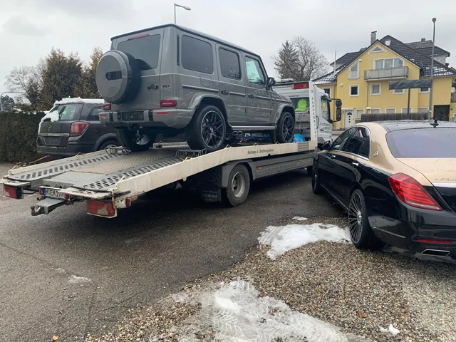 Grauer Mercedes-AMG G63 vor einem beladenen Fahrzeuganhänger