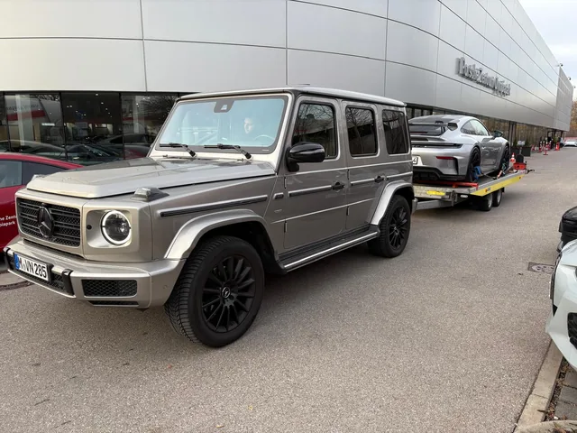 Grauer Mercedes-AMG G63 vor einem Porsche 911 GT3 auf dem Anhänger